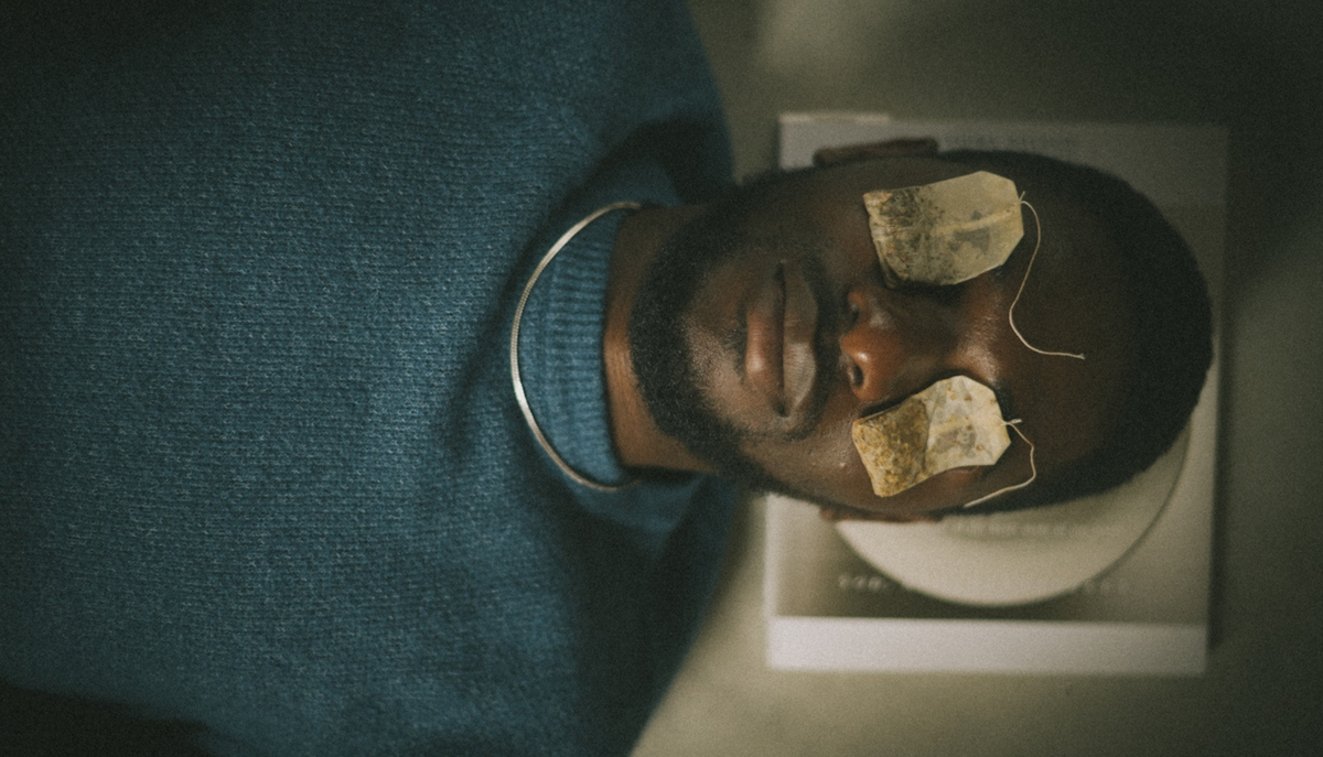 A man laying down with steeped tea bags over his eyes