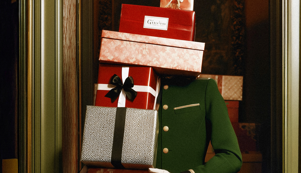 A tall stack of wrapped and unwrapped holiday gifts being carried by someone in a classic doorman outfit