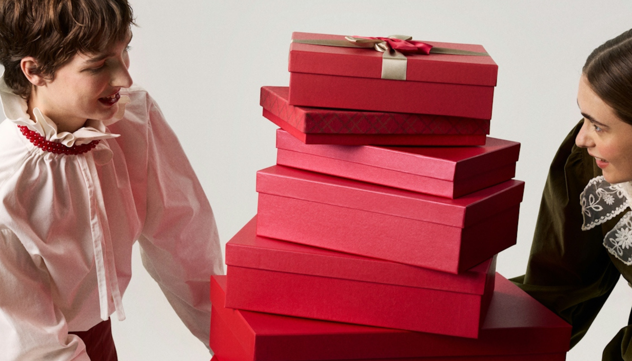 Two_people_marvelling_at_a_tall_stack_of_presents_in_red_boxes_between_them