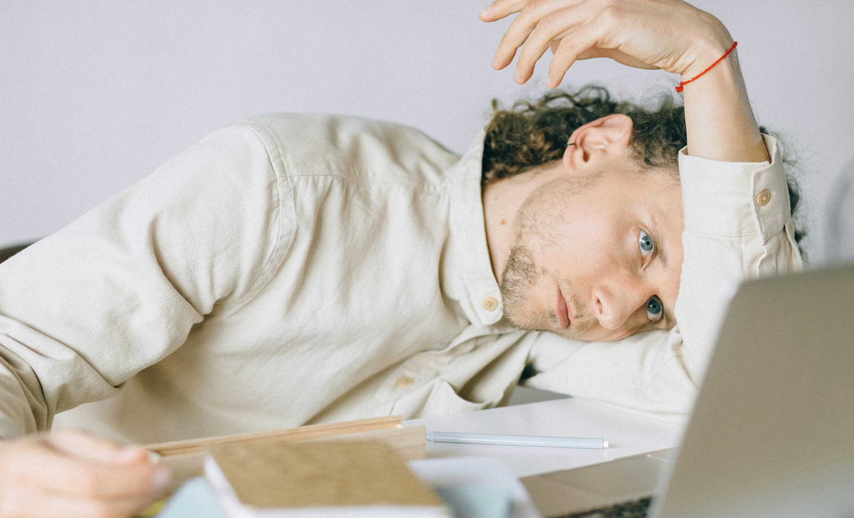 A man slumped over to the side and resting his head on his arm, looking distressed about the work in front of him
